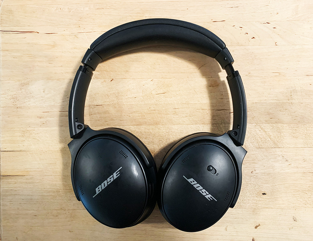 A pair of black Bose Quiet Comfort 45 headphones against a wooden background.