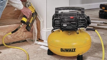 A man while repairing a yellow DEWALT electric air compressor with a round body and its engine on it and a black cable.