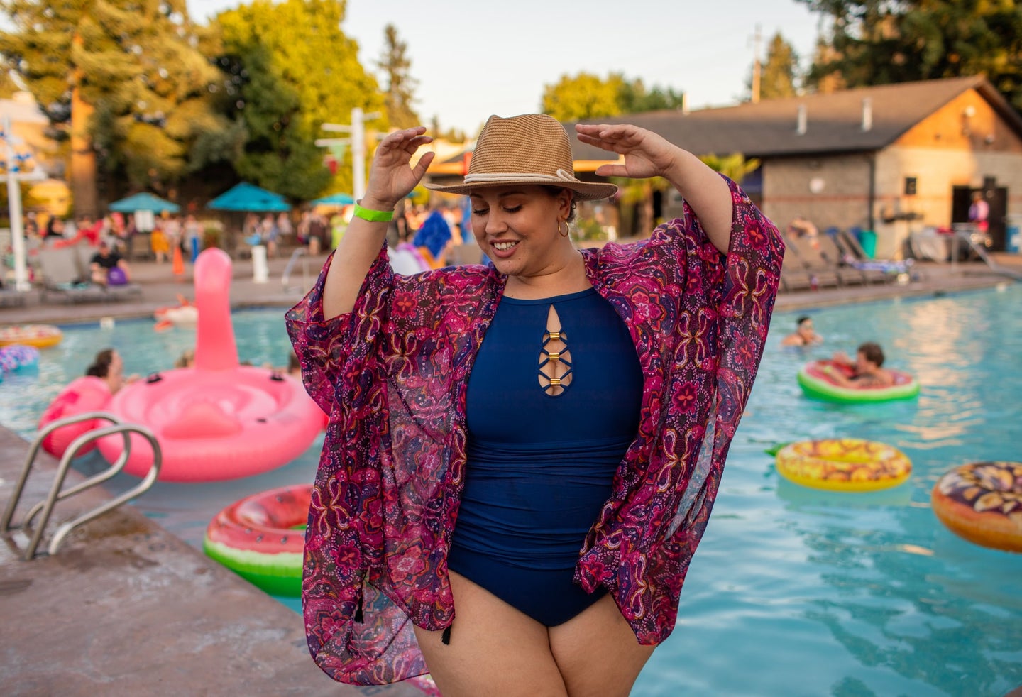 Person in blue one-piece bathing suit, sun hat, and pink kimono at pool