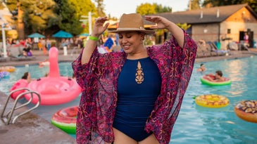 Person in blue one-piece bathing suit, sun hat, and pink kimono at pool