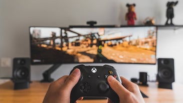 Hands holding XBox controller in front of a large computer monitor