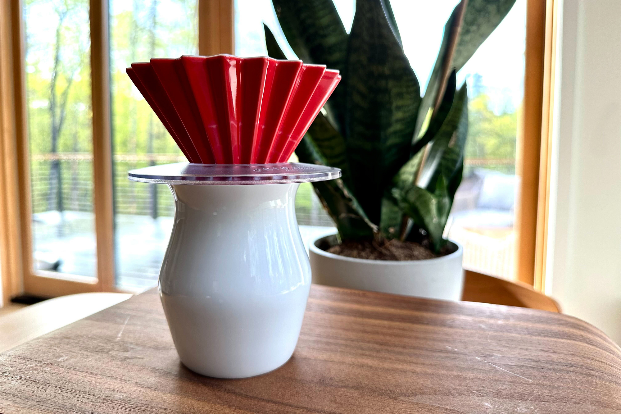 Red ceramic Origami pour-over dripper on a table with a snake plant
