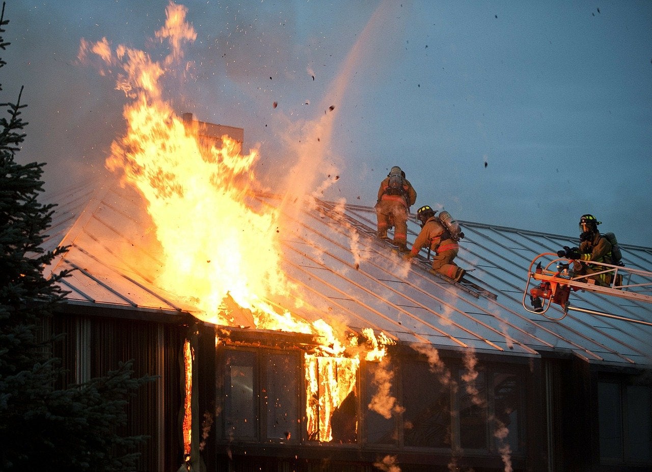 Firefighters battle a fire while climbing on a roof.