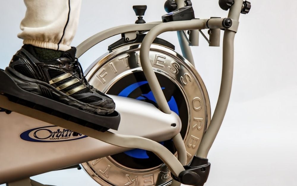 A foot of a person wearing sports sneakers who is pedaling on a black and white fitness machine.