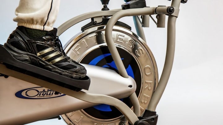 A foot of a person wearing sports sneakers who is pedaling on a black and white fitness machine.