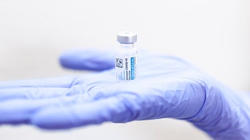 A blue-gloved hand holds a vial of the Johnson & Johnson/Janssen COVID-19 vaccine.