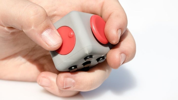 A person's hand as he presses a gray square cube with red buttons on it.