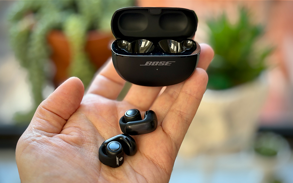 Black Bose Ultra Open earbuds in my palm holding their open case