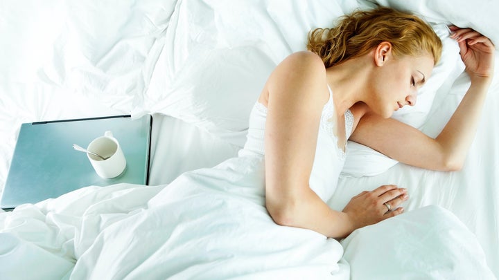 Woman sleeping in bed next to laptop and empty mug
