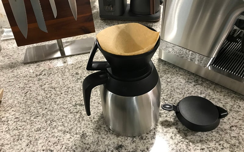 Melitta steel carafe pour-over coffee maker with filter on a counter with kitchen knives and other coffee machines