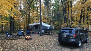Pop-up camper in the woods next to an SUV and firepit