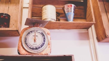 An old wooden weight gauge placed on a wooden drawer below some other drawers.