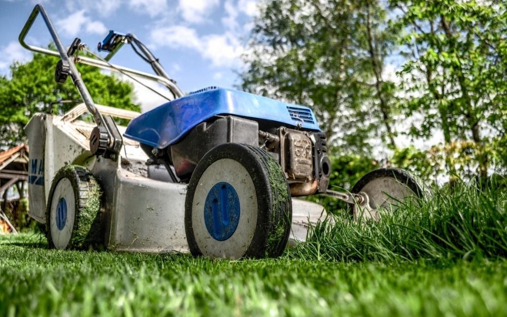 A grey and blue lawn mower photographed from its tire corner, on a field of green grass.