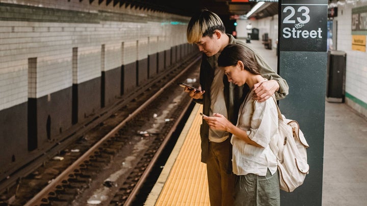 Couple waits by the NYC train platform looking at their phones
