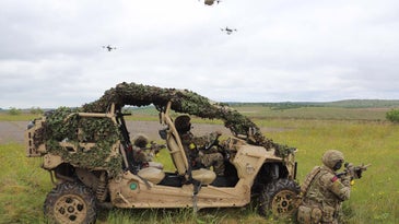 soldiers near a vehicle with drones in the background