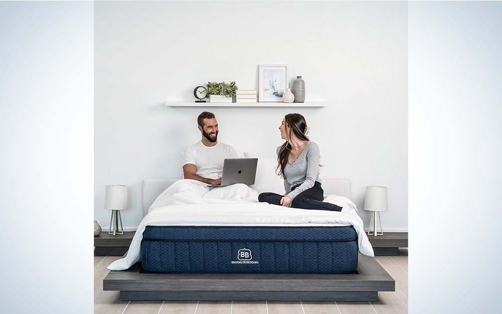 A man with a laptop and a woman sitting on a Brooklyn Bedding mattress.
