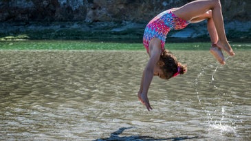 Kid in pink bathing suit doing a flip in a lake