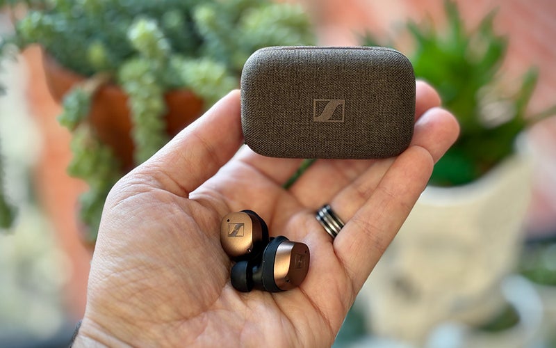 Copper-black Sennheiser MOMENTUM True Wireless 4 earbuds held in my hand with their fabric-covered case