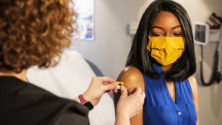 a woman gets a vaccine while wearing a yellow mask