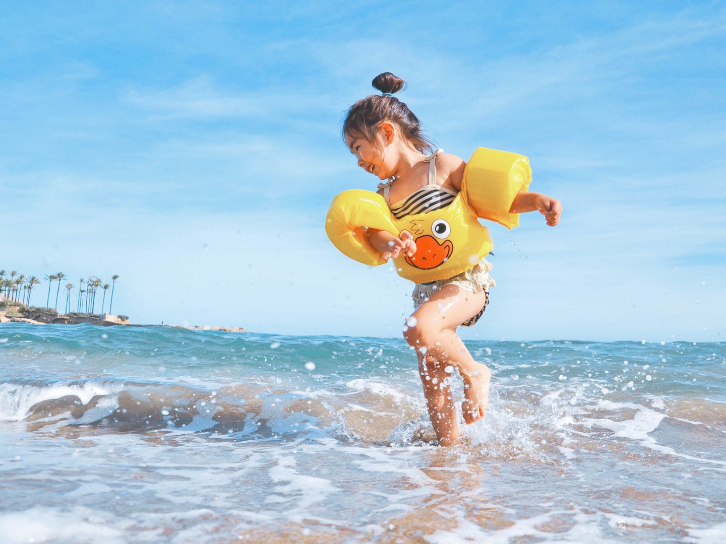 A small child wearing floaties on their arms and waist while playing in the surf of a tropical beach.
