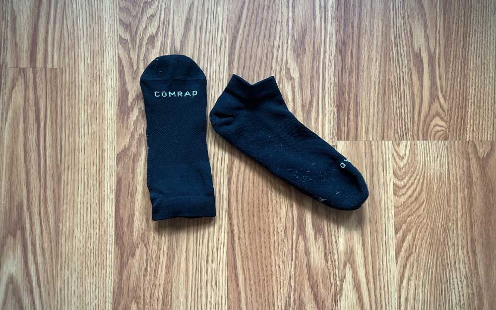 A black pair of Comrad ankle compression socks on a wooden floor.