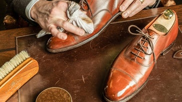 Hands polishing fancy leather shoes on a fancy wooden table.