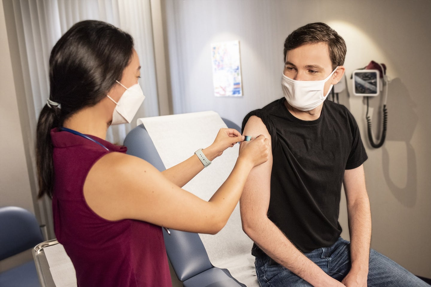 A woman gives a COVID-19 vaccine shot to a young person while both wear masks