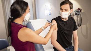 A woman gives a COVID-19 vaccine shot to a young person while both wear masks