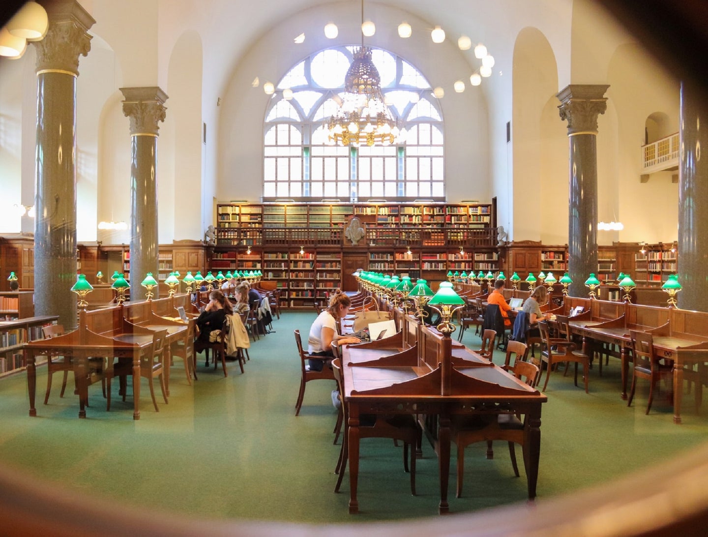 College library with students at tables and green lamps