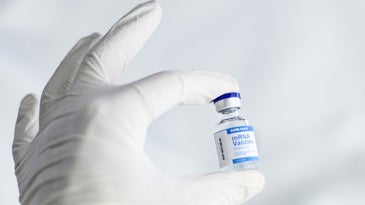 A gloved hand holds a vial of COVID vaccine.