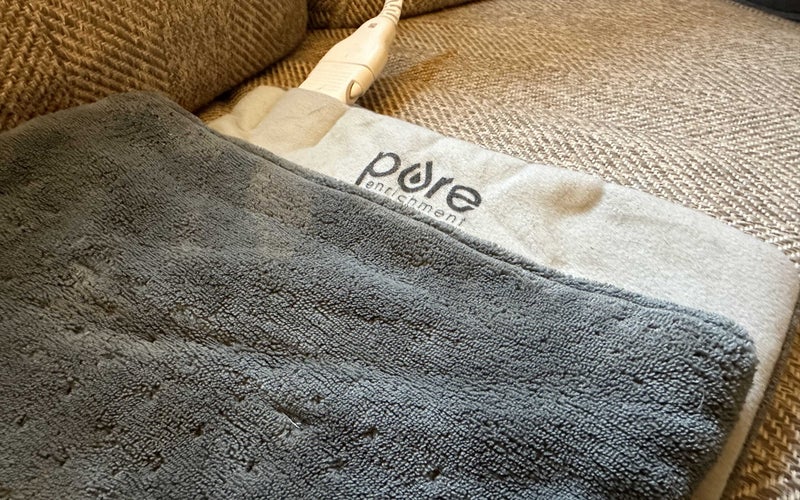 A gray heating pad made by Pure Enrichment with some cords on a couch