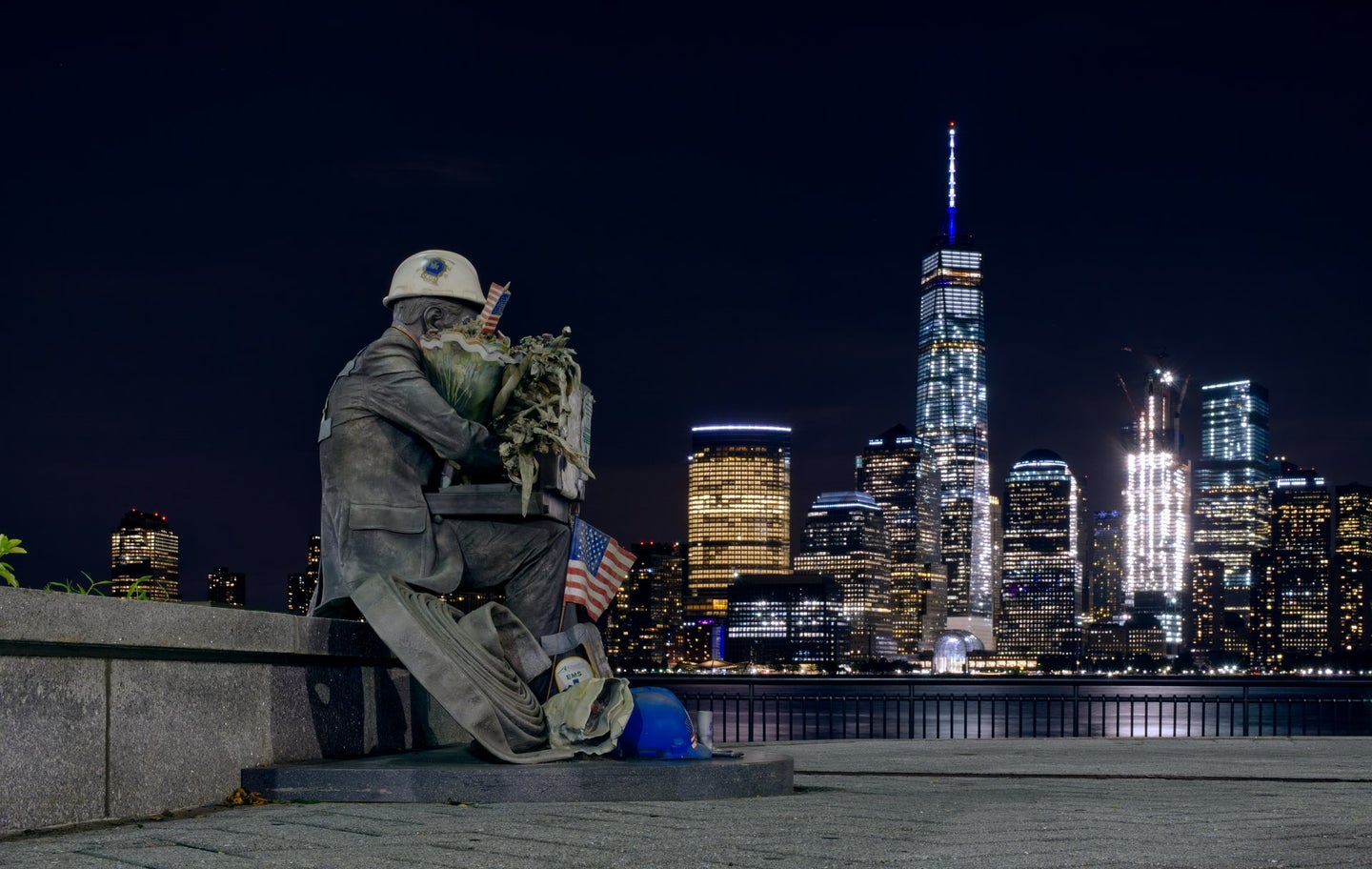 a statue of a firefighter sits with the One World Trade Center tower in the background
