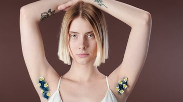 A blonde woman in a white top with her arms above her head and flowers in her armpits.