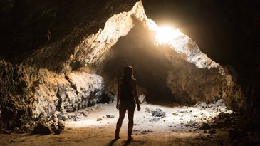 Person with long hair looking at sun through cave
