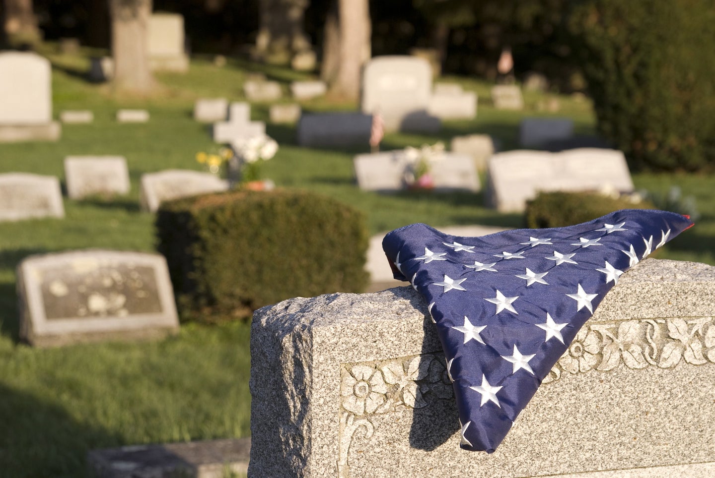 A folded American flag rests on top of a grave stone, with other gravestones in the background.