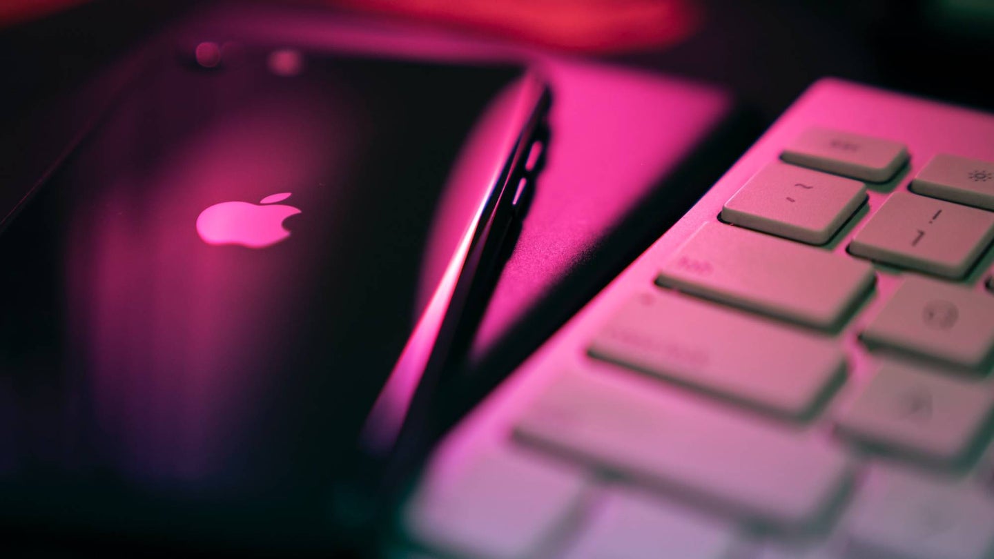 An iPhone and a Mac computer keyboard illuminated under a pink light.
