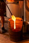 A bucket full of molten glass with a rod dripping some orange liquid glass