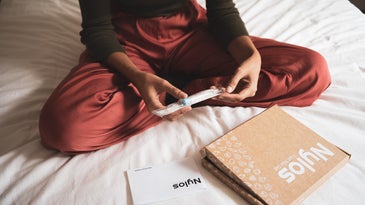 Person in red pajamas holding a pregnancy test on a bed