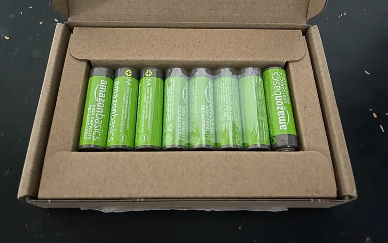 An open cardboard box displaying eight green AmazonBasics batteries next to each other through an open panel
