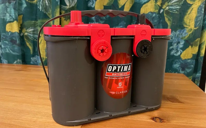 An Optima Redtop 12V battery with a gray body and red top sitting on a table.