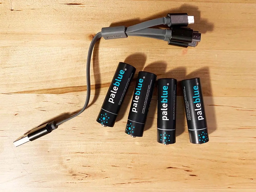 Four Pale Blue AA batteries on a table next to a four-pronged charger.
