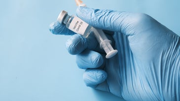 A gloved hand holding a syringe and vial.