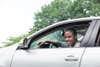 Black teen smiling in the driver's seat of a silver car