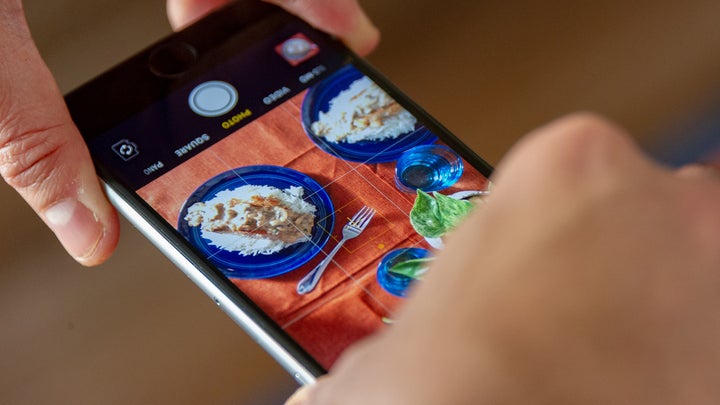 A person using their iPhone to take a photo of some food on a table.