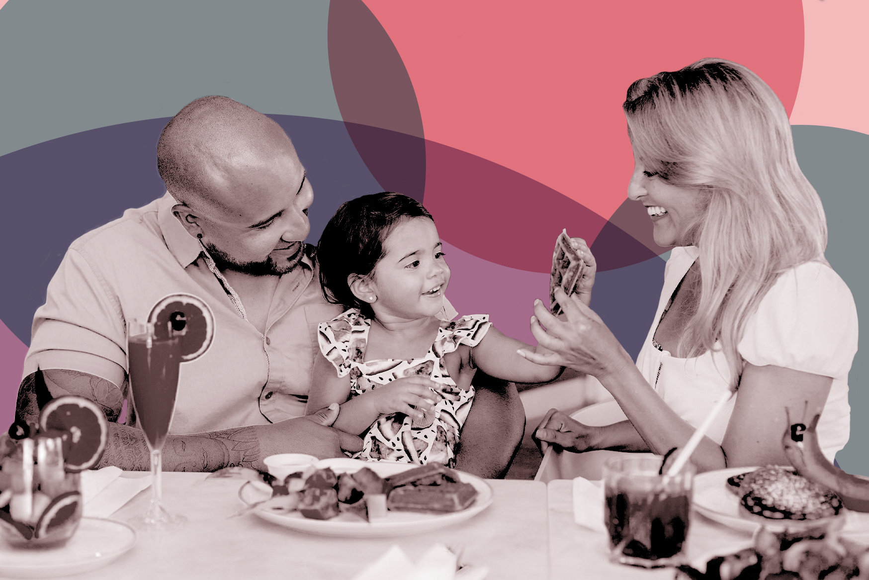 two adults sit at a table full of food with a small child as they smile