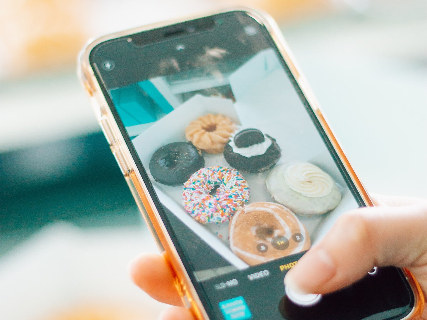 A person holding an iPhone and taking a picture of some doughnuts.