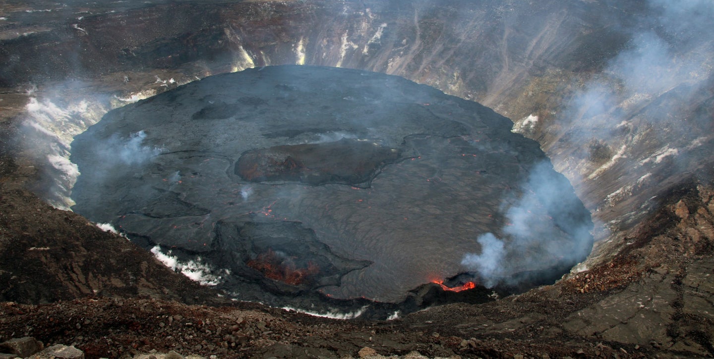 A large black crater in a volcano with smog and lava