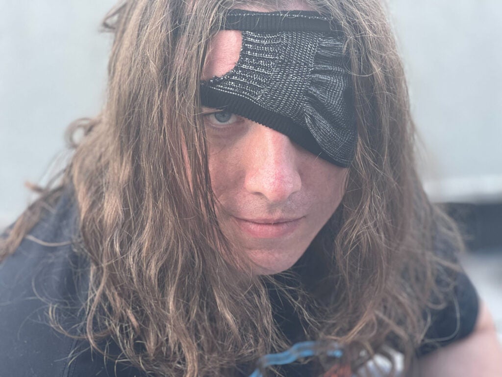 A man with long hair wearing a face mask as an eye patch.