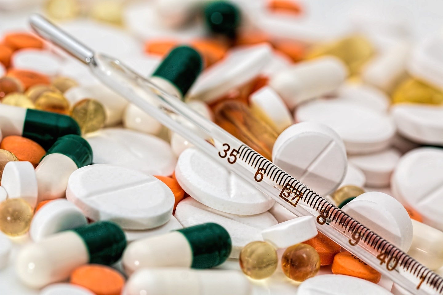Green, white, and orange pills & thermometer to symbolize COVID-19 symptoms and treatments