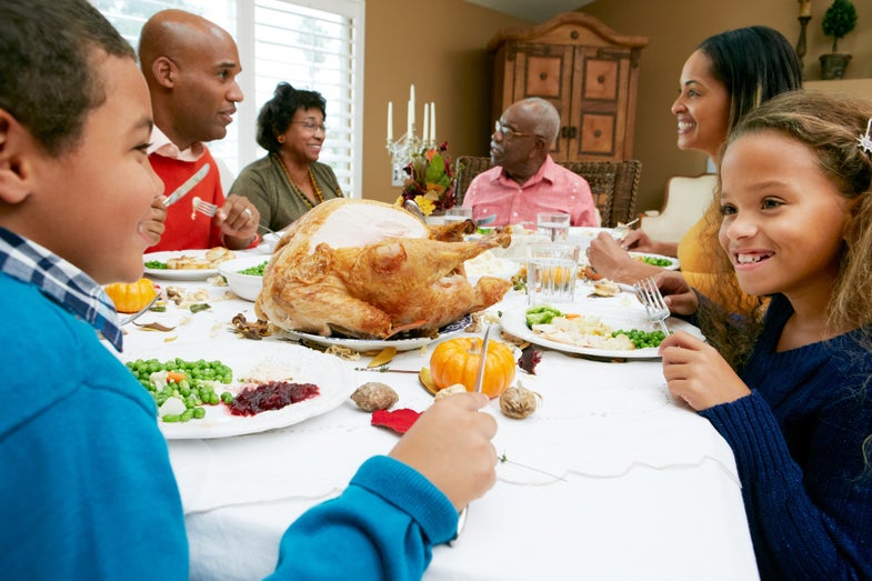 Black family with kids and seniors beating back holiday stress around a white dinner table
